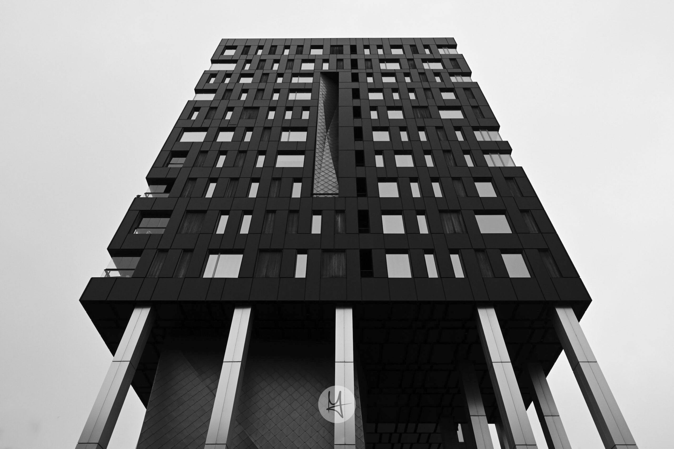 A striking black-framed building in Tallinn, Estonia, featuring a multi-faceted geometric facade composed of dark panels. The building rises on a concrete base with slender, dark supports. Captured from a low-angle perspective, the photo emphasizes the building’s height and complex form, contrasting with the surrounding urban environment.