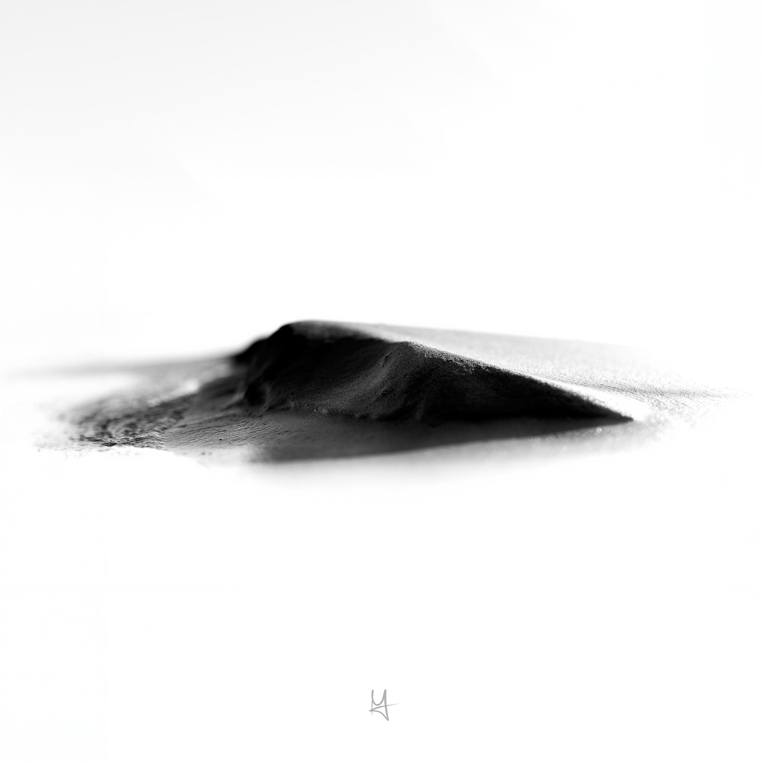 A black and white photo of a very very small „dune“ at the beach. It's a macro photo of some sand in bright sunlight. Most part of the photo is white.