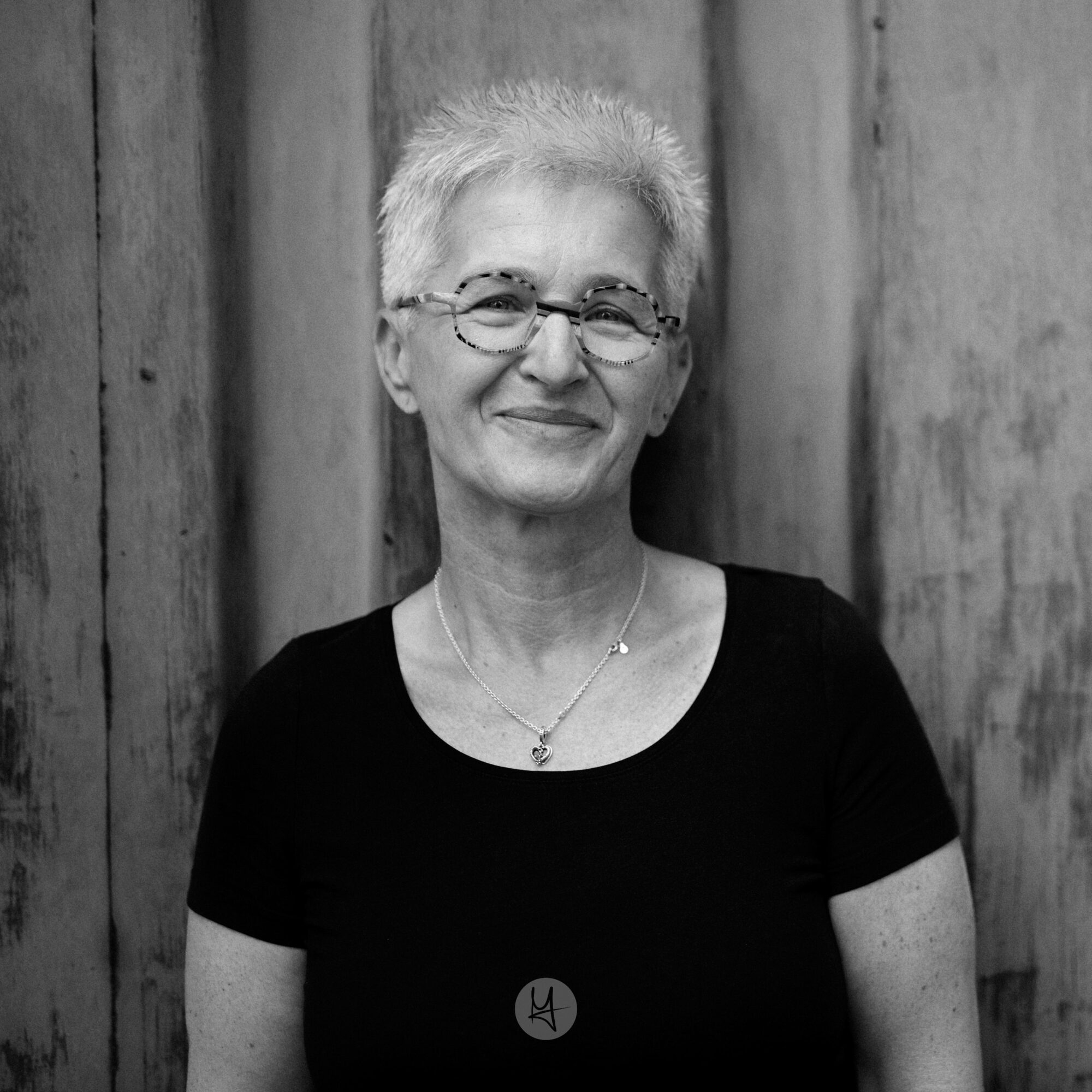 A portrait of a woman standing in front of an old and rusty garage door. Smiling.