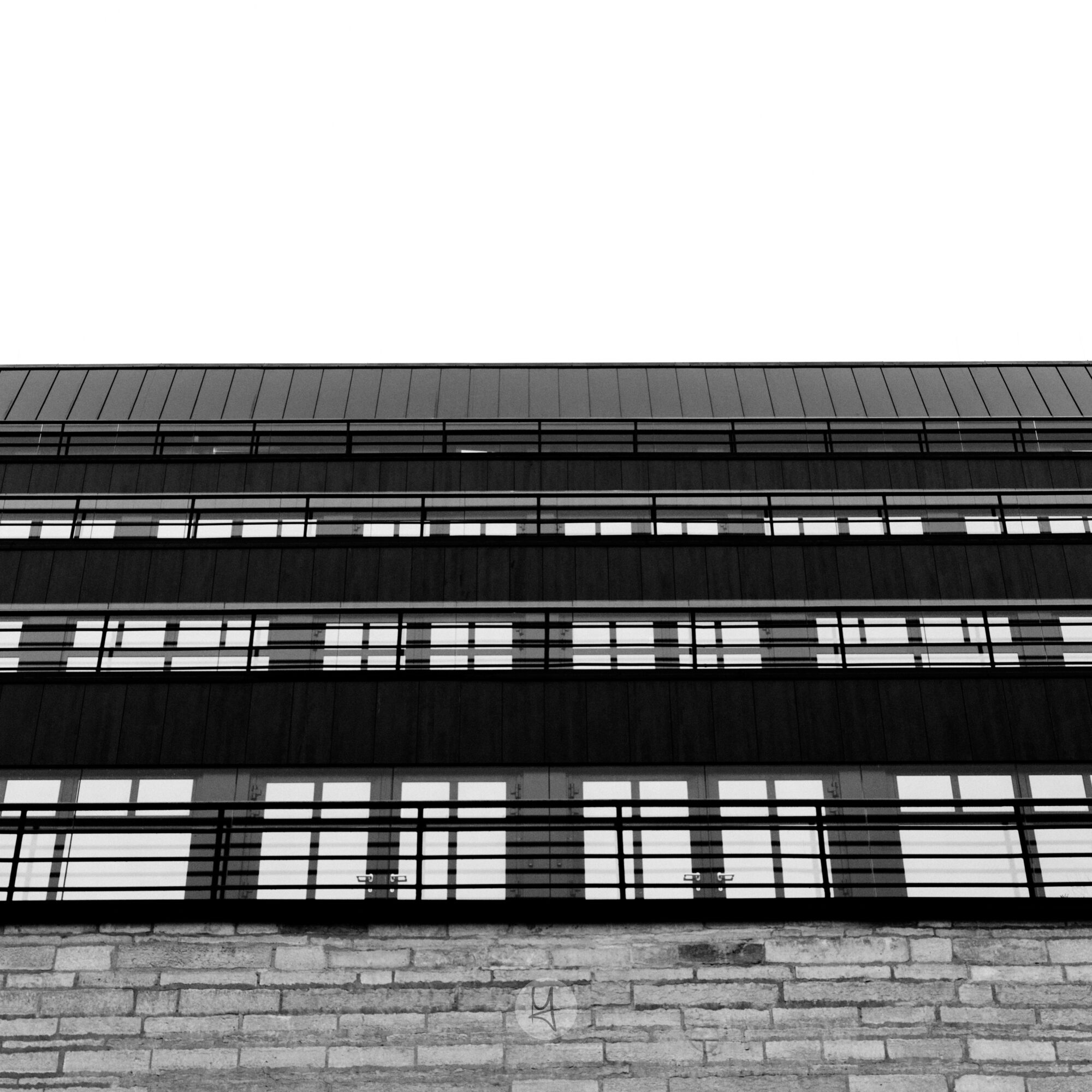 Ein Blick auf die neue National Bibliothek von Estland in Tallinn. Die Seiten des Gebäudes sind auf mehreren Etagen mit Fenstern ausgestattet. Das schwarz-weiße Foto hat eine Froschperspektive mit einem nach oben gerichteten Winkel auf die Fensterfront. Im unteren Teil ist ein Mauerwerk zu erkennen. Die Fenster ergeben ein regelmäßiges Muster.