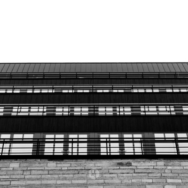 Ein Blick auf die neue National Bibliothek von Estland in Tallinn. Die Seiten des Gebäudes sind auf mehreren Etagen mit Fenstern ausgestattet. Das schwarz-weiße Foto hat eine Froschperspektive mit einem nach oben gerichteten Winkel auf die Fensterfront. Im unteren Teil ist ein Mauerwerk zu erkennen. Die Fenster ergeben ein regelmäßiges Muster.