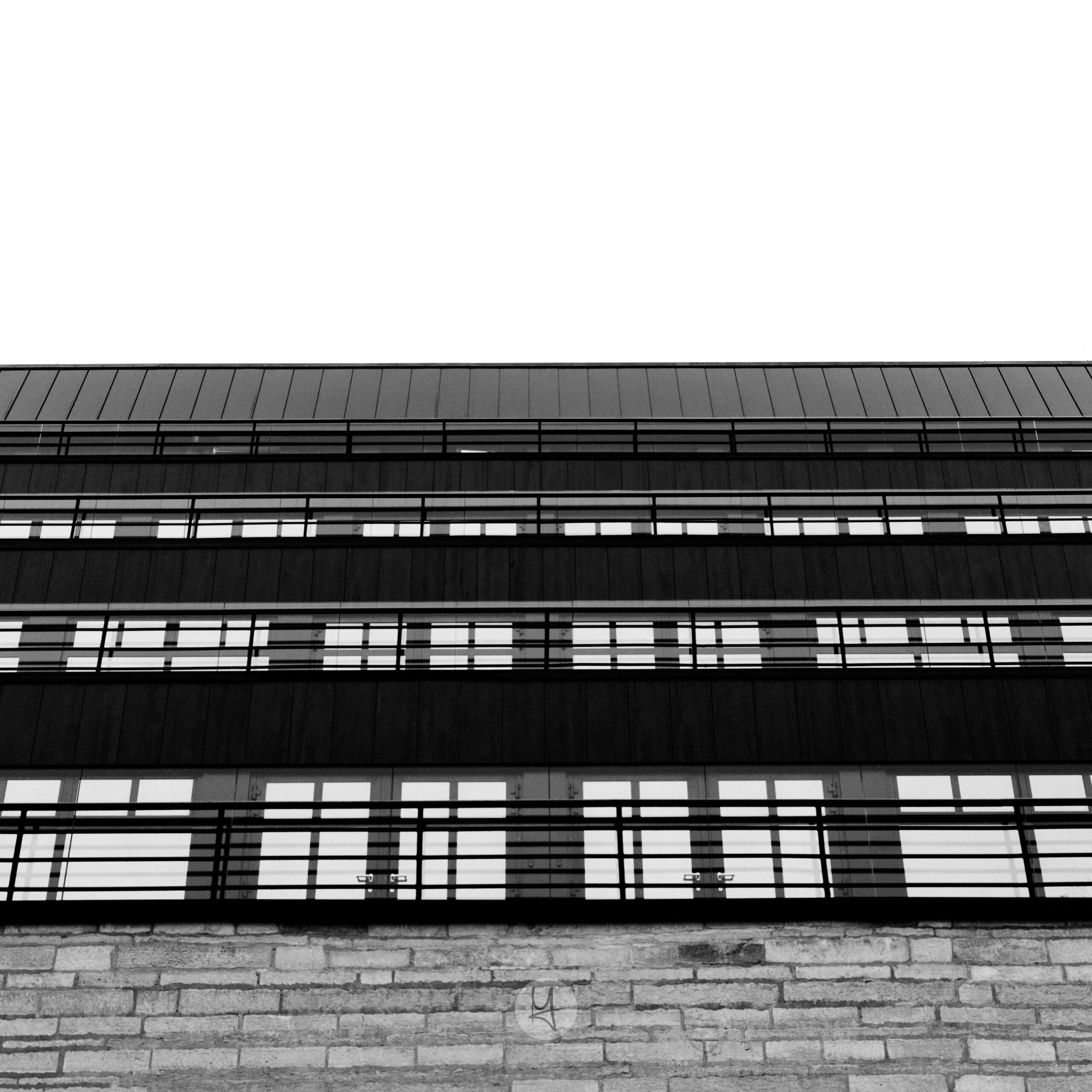 Ein Blick auf die neue National Bibliothek von Estland in Tallinn. Die Seiten des Gebäudes sind auf mehreren Etagen mit Fenstern ausgestattet. Das schwarz-weiße Foto hat eine Froschperspektive mit einem nach oben gerichteten Winkel auf die Fensterfront. Im unteren Teil ist ein Mauerwerk zu erkennen. Die Fenster ergeben ein regelmäßiges Muster.