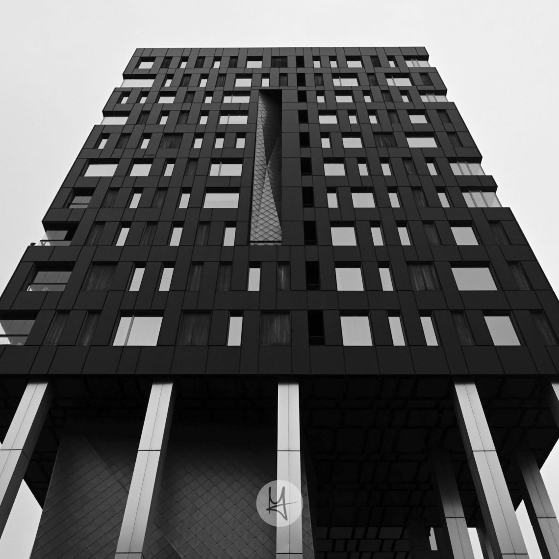 A striking black-framed building in Tallinn, Estonia, featuring a multi-faceted geometric facade composed of dark panels. The building rises on a concrete base with slender, dark supports. Captured from a low-angle perspective, the photo emphasizes the building’s height and complex form, contrasting with the surrounding urban environment.