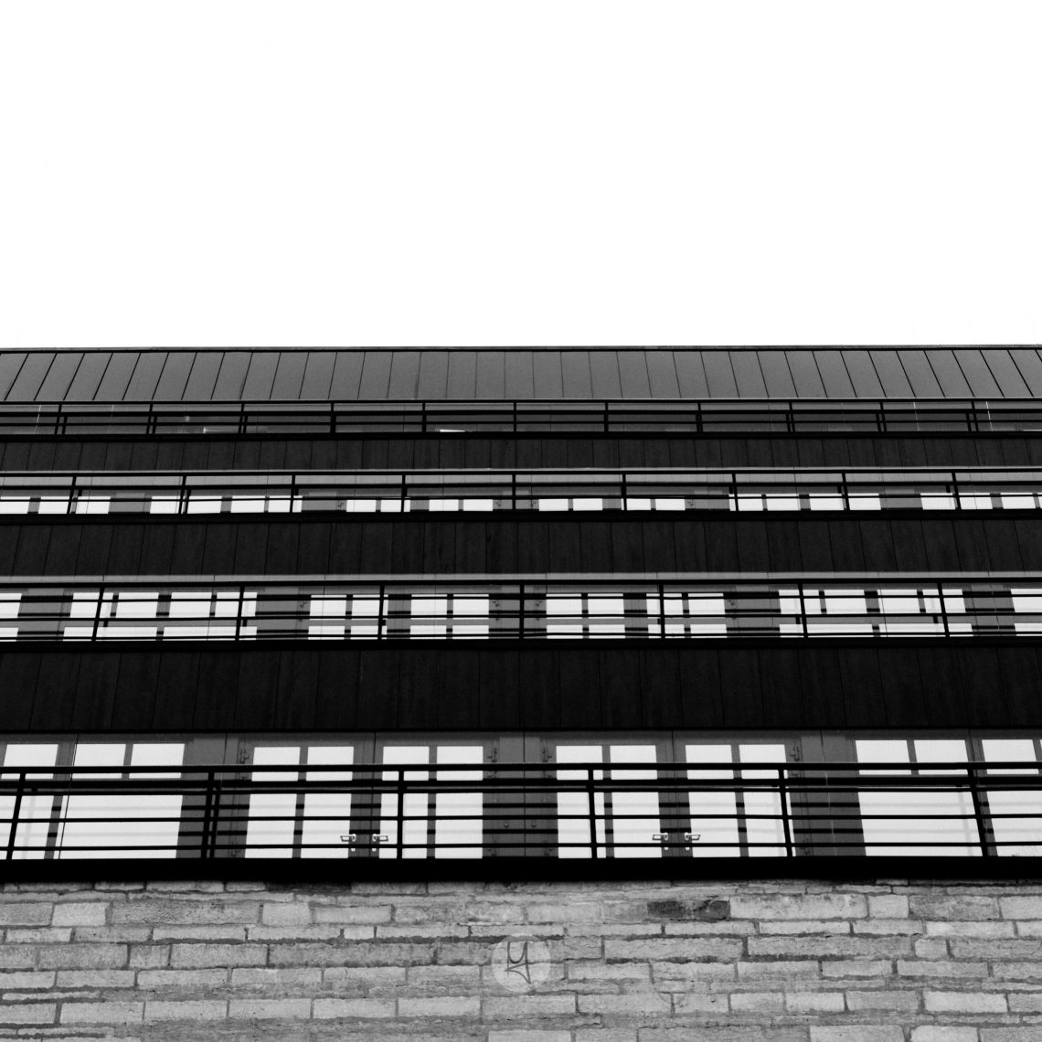 Ein Blick auf die neue National Bibliothek von Estland in Tallinn. Die Seiten des Gebäudes sind auf mehreren Etagen mit Fenstern ausgestattet. Das schwarz-weiße Foto hat eine Froschperspektive mit einem nach oben gerichteten Winkel auf die Fensterfront. Im unteren Teil ist ein Mauerwerk zu erkennen. Die Fenster ergeben ein regelmäßiges Muster.